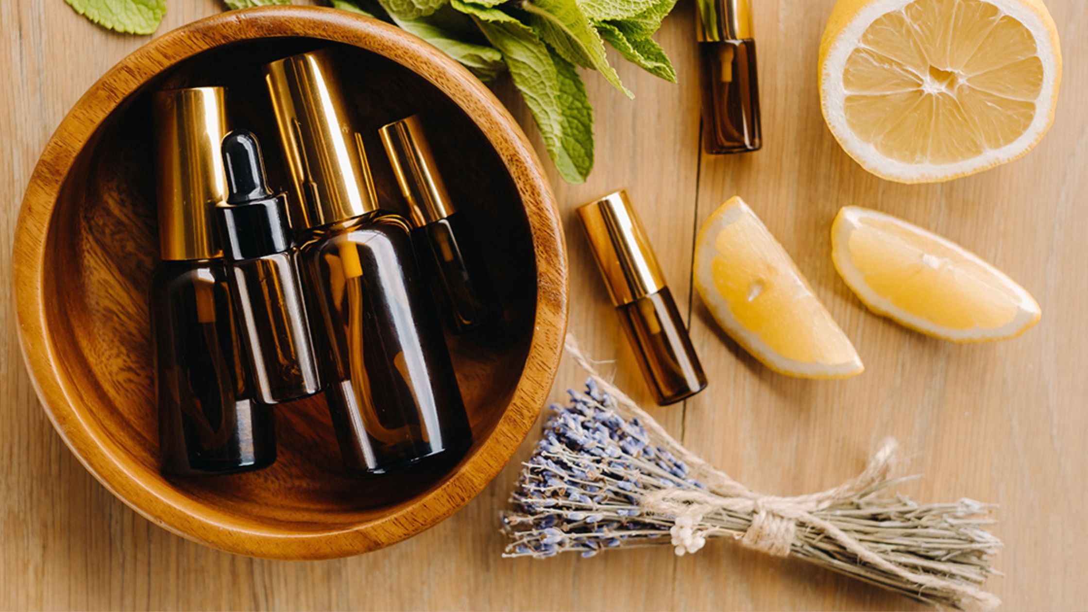 A wooden bowl filled with essential oil bottles, surrounded by fresh lemon slices, mint leaves, and lavender sprigs, representing the natural essence of aromatherapy.